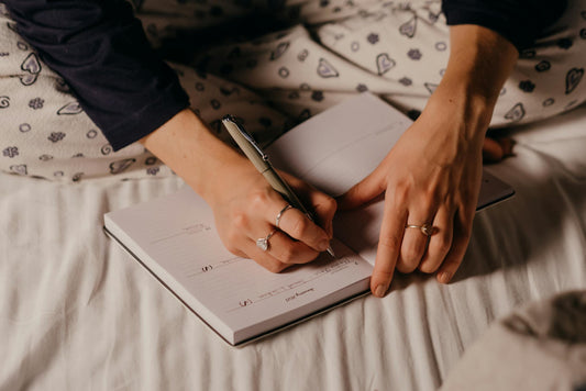 A person's hands writing in a journal at night, with a warm, cozy light.